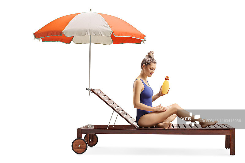 一名年轻女性正在涂抹防晒霜，并打着伞站在日光浴床上图片素材