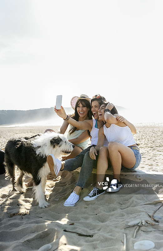快乐的女性朋友和狗在海滩上自拍图片素材