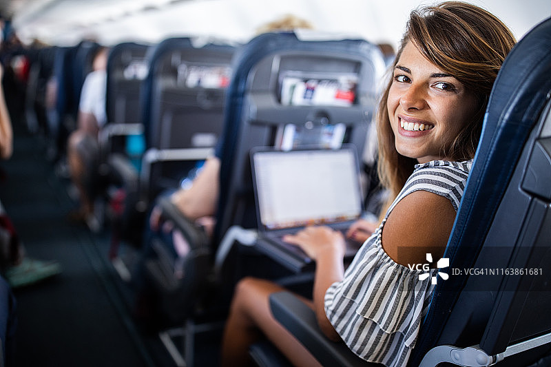 快乐的女人在乘飞机旅行时使用电脑。图片素材