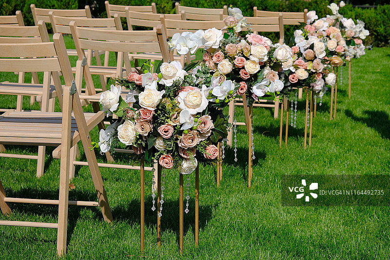 白色木制空椅子排成一排，绿色草地上放着花束。婚礼装饰。图片素材
