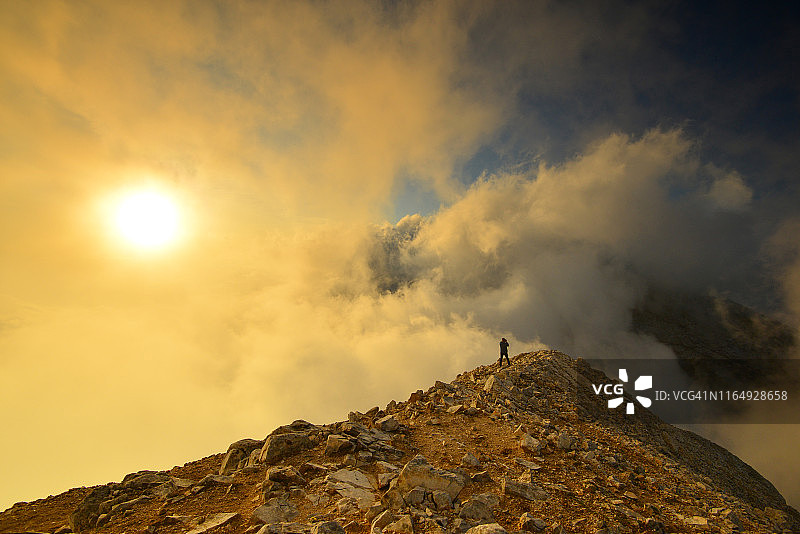 一个孤独的人站在山脊上，在日落时被云包围图片素材