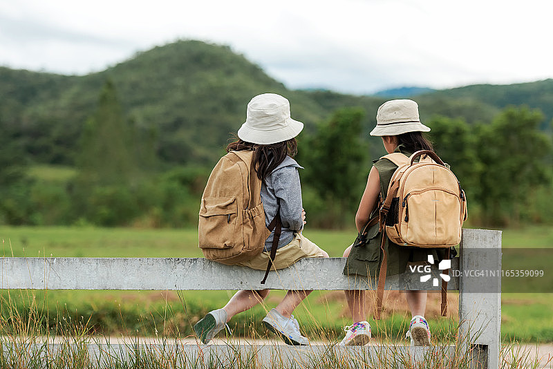 亚洲的两个孩子坐在户外的白色围栏上，冒险和旅游目的地与山休闲旅行，教育和放松的户外自然公园。旅游度假的概念图片素材