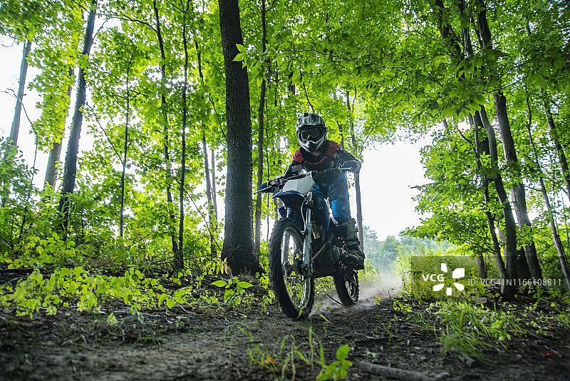 一个骑越野摩托车的人骑着摩托车在树林里。图片素材