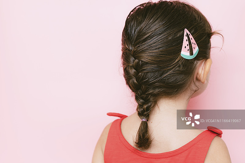 小女孩的背影与辫子和发夹在粉红色的背景图片素材