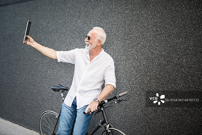 快乐的老人靠在自行车上自拍。图片素材