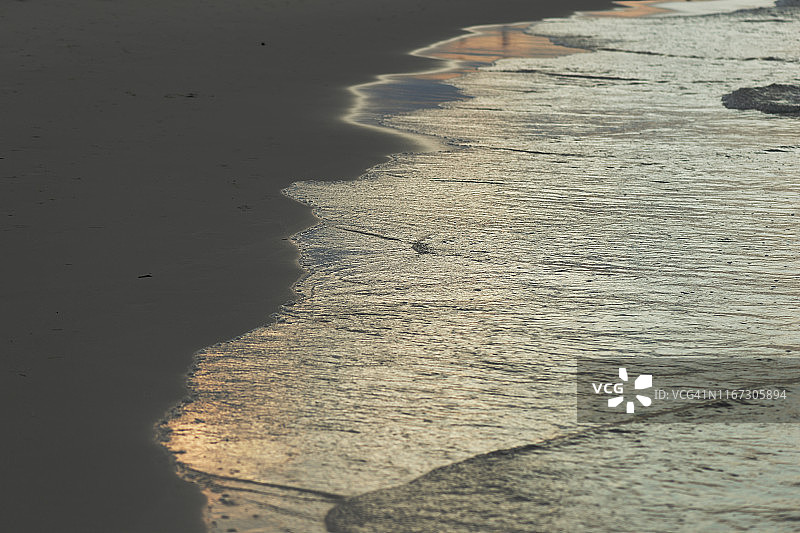 海滩上潮湿的沙子被黄昏的太阳照亮。自然的抽象背景图片素材