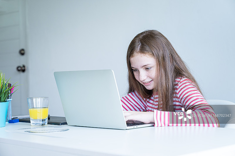可爱的小女孩坐在客厅里使用笔记本电脑。图片素材