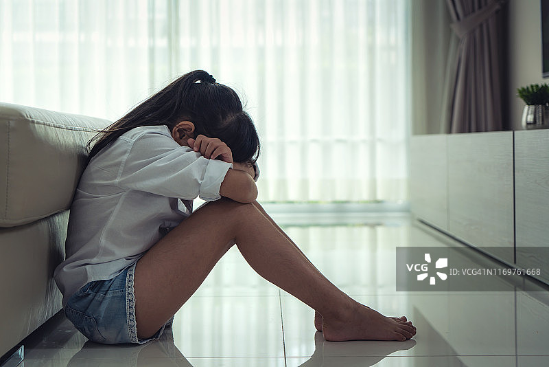 沮丧的亚洲小女孩坐在地板上拥抱她的膝盖在悲伤的穆迪在家里。她感到孤独和悲伤。图片素材