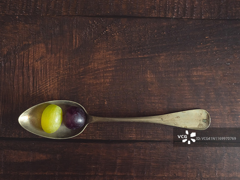 秋季水果:一个老羊驼勺子，上面有一颗白葡萄和一颗黑葡萄图片素材