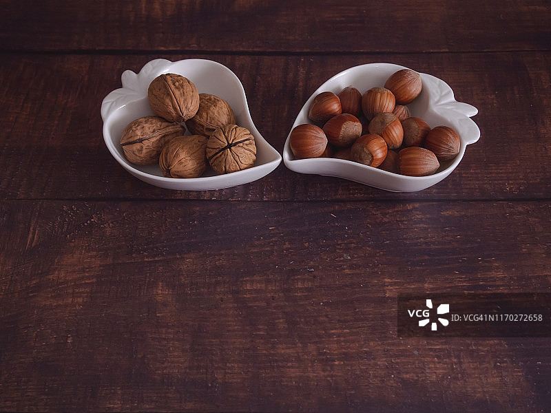 秋果:两组坚果和榛子，放在一个旧木桌上的心形瓷碗里图片素材