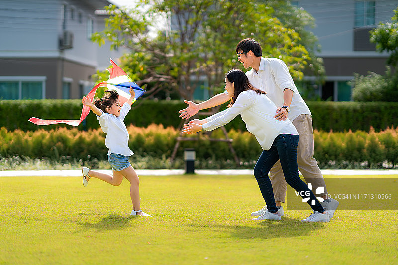 亚洲女儿跑到妈妈和爸爸，她喜欢和家人在公园里玩风筝。图片素材