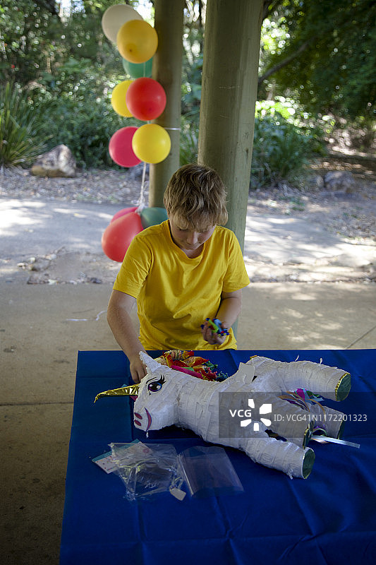 一个8岁的男孩给独角兽吃棒棒糖piñata图片素材