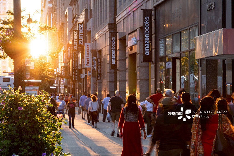阳光照耀着形形色色的人群，他们走过纽约市34街的人行道上的商店和商店图片素材
