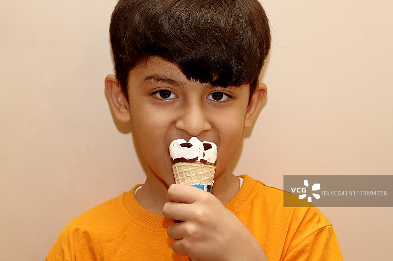一个小男孩一边吃蛋筒冰淇淋一边看着相机图片素材