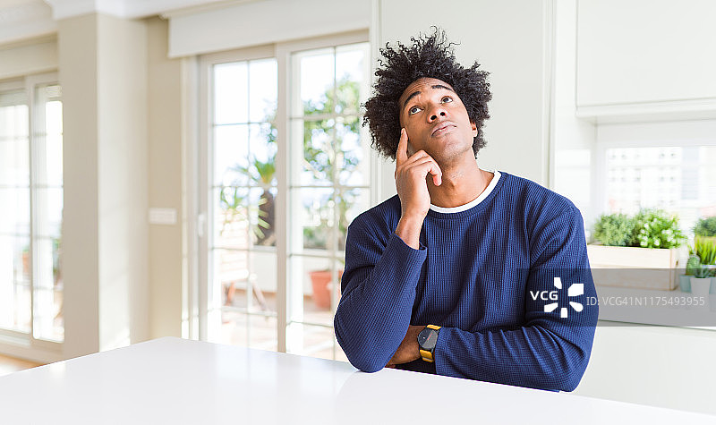 年轻的非洲裔美国人穿着休闲毛衣坐在家里，手放在下巴思考问题，沉思的表情。带着沉思的微笑。怀疑的概念。图片素材