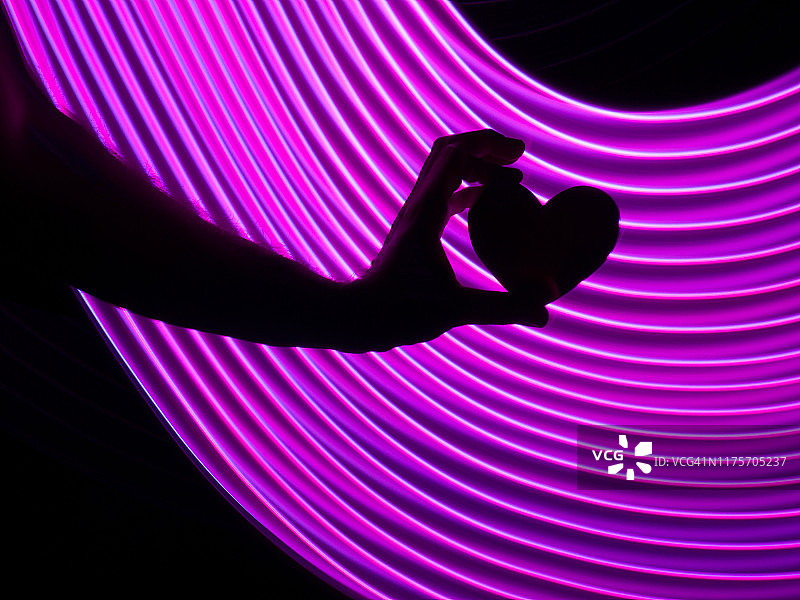 在一个粉色的虚拟环境中，人类的手握着一颗心。图片素材