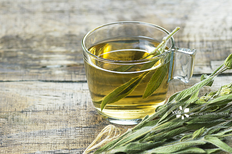 玻璃杯的草药鼠尾草茶与干鼠尾草叶子在木制的乡村背景。凉茶概念热饮，丹参图片素材