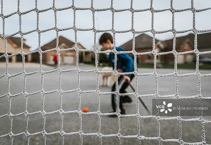 一个小男孩用一根曲棍球棍打过网的球。图片素材