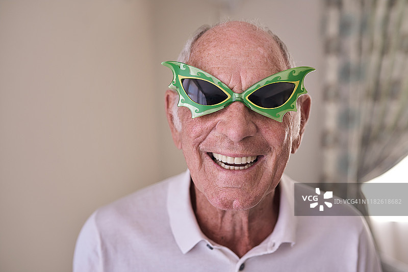 微笑的老人戴着幽默的红色新奇眼镜图片素材