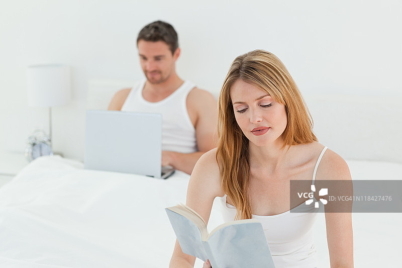 男人在玩笔记本电脑，而他的妻子在看书图片素材