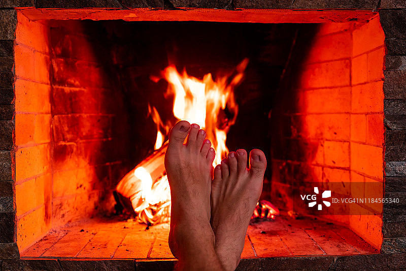 男人的脚在壁炉的背景火特写图片素材