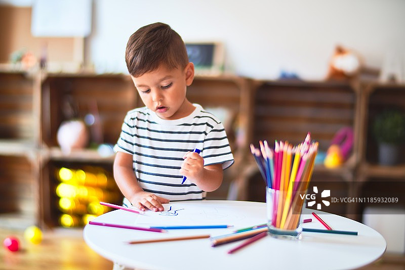 美丽的蹒跚学步的男孩在幼儿园用彩色铅笔画可爱的画图片素材