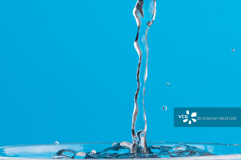 在玻璃杯里洒点水。两滴水的碰撞效果。蓝色背景。图片素材