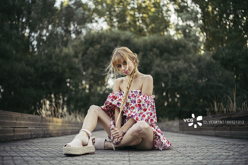 年轻女子的肖像，穿着夏季连衣裙与花卉设计坐在木板路图片素材