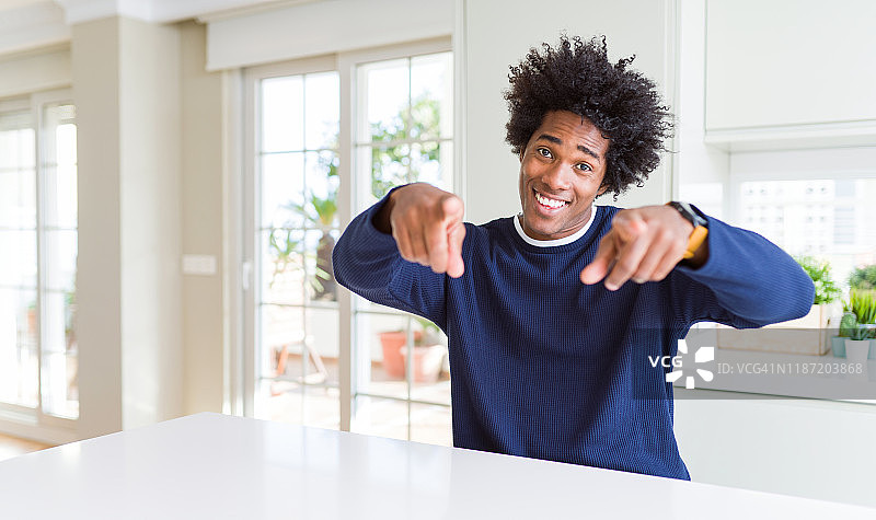 年轻的非裔美国人穿着休闲毛衣坐在家里用手指指着你和相机，微笑着积极和愉快图片素材