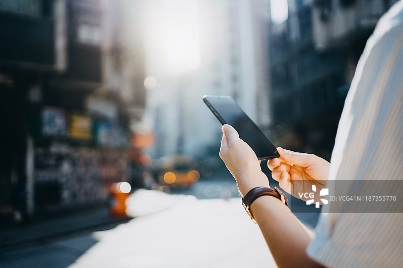在美丽的阳光下，一个女人在城市中使用智能手机，背景是城市摩天大楼和交通图片素材