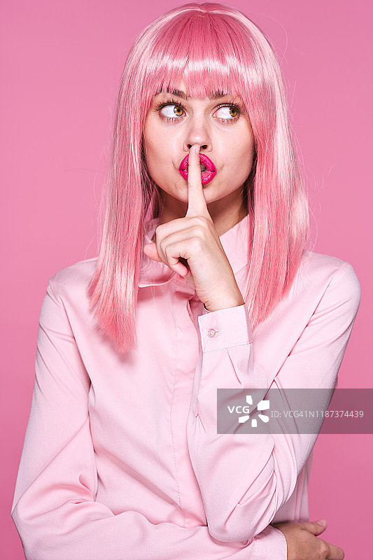 粉红色背景上的粉红色头发的漂亮女孩显示出“安静”的标志图片素材