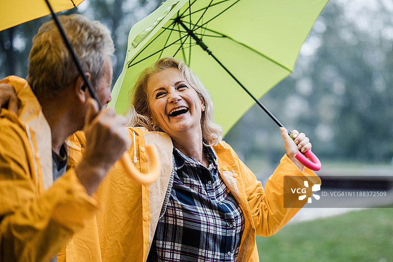 一对穿着黄色雨衣的快乐成熟的夫妇在雨伞下聊天。图片素材