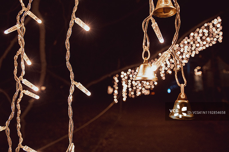 金色的圣诞装饰灯与闪亮的花环和小金属铃铛在黑暗的背景与散景灯。挂照明。新年庆祝背景与拷贝空间。图片素材