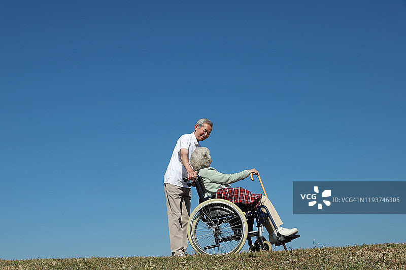 老年男子协助坐轮椅的老年妇女图片素材