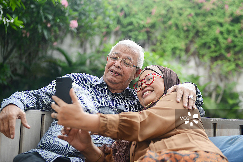 一对快乐微笑的印尼老年夫妇坐在家里的木凳上图片素材