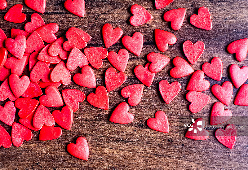 情人节背景与红心木桌子上，俯视图。红色的心型糖果在木制的棕色背景上。情人节的概念。图片素材