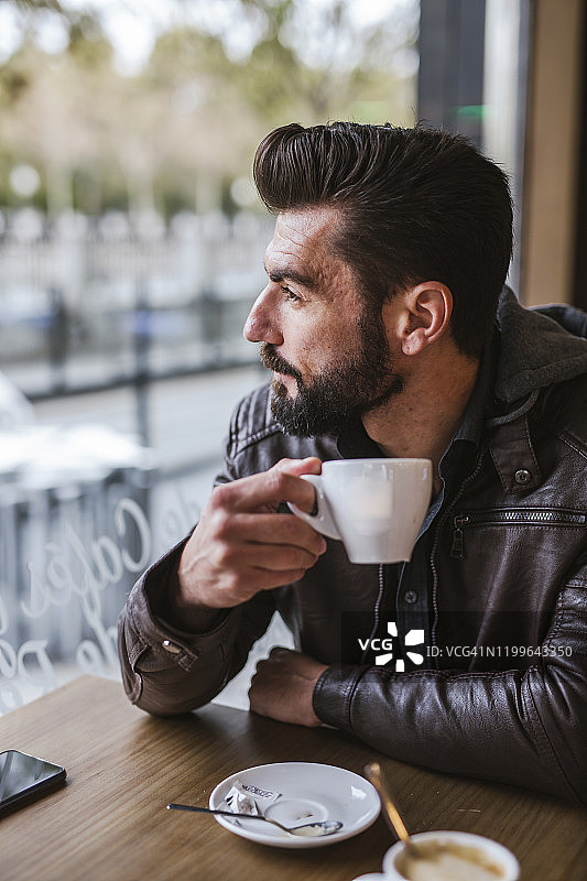 一个满脸胡须的成熟男子在咖啡店里望着窗外图片素材