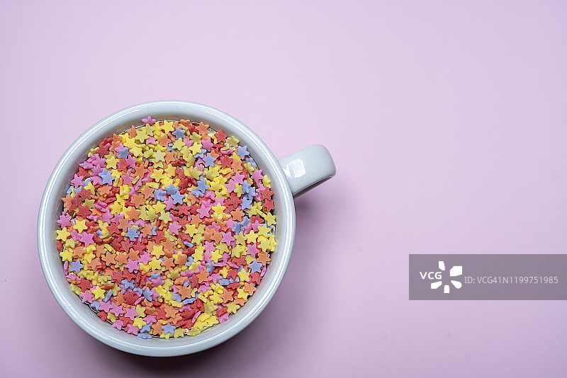 彩色的糖星星在杯子上粉红色的背景图片素材