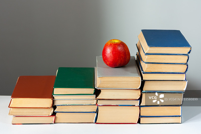 白色的桌子上放着红苹果，上面放着精装书。书堆积。回到学校的概念。副本的空间。教育学习背景图片素材