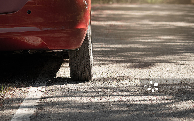 一辆红色轿车的后轮轮胎停在柏油路边。图片素材