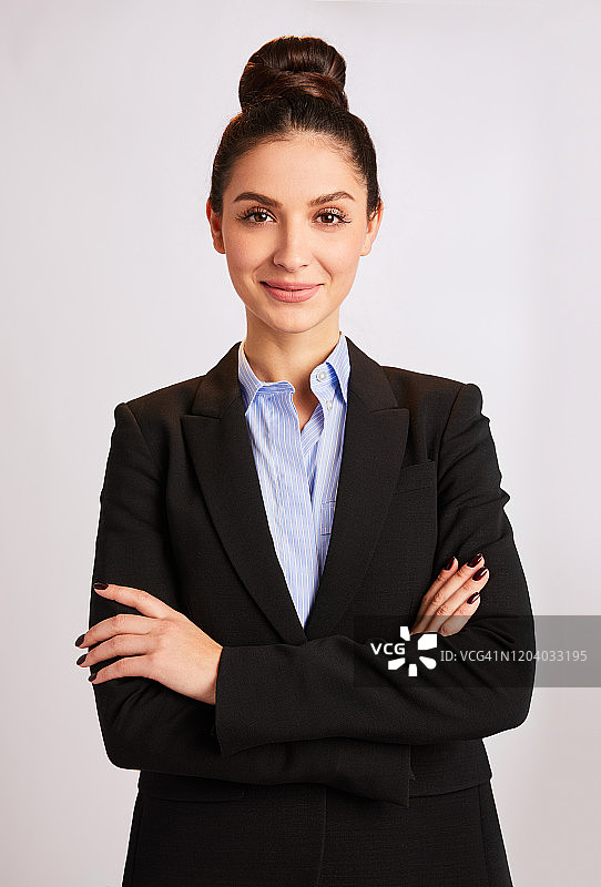微笑的女商人站在灰色的背景，她的双臂交叉图片素材