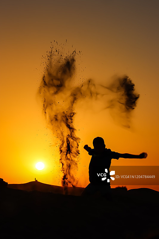 小男孩在迪拜沙漠撒沙子的日落剪影图片素材