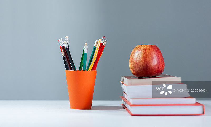 橙色的铅笔盒，打开的精装书，日记本，扇形的书页堆在白色的桌子上，上面放着红苹果。书堆积。回到学校的概念。副本的空间。教育学习背景图片素材