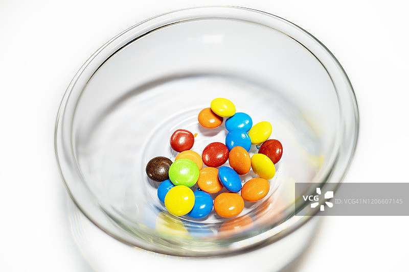 玻璃碗和彩色的巧克力豆在白色的背景图片素材