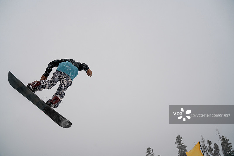 在一个下雪天，一个年轻的男性滑雪运动员在科罗拉多州的一个滑雪场跳下来图片素材