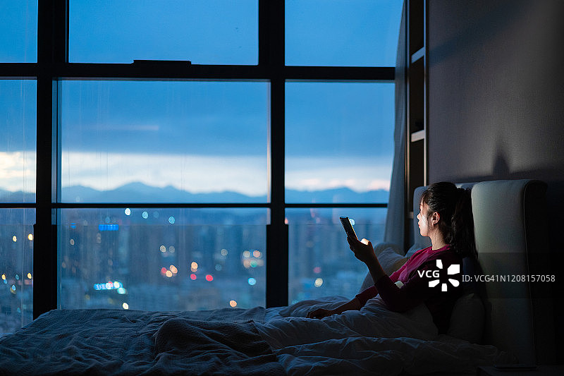 亚洲女性在床上使用智能手机图片素材