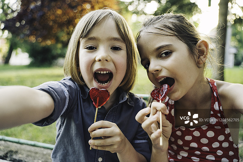 两个孩子一边自拍一边吃棒棒糖。孩子们在公园里玩得很开心。图片素材