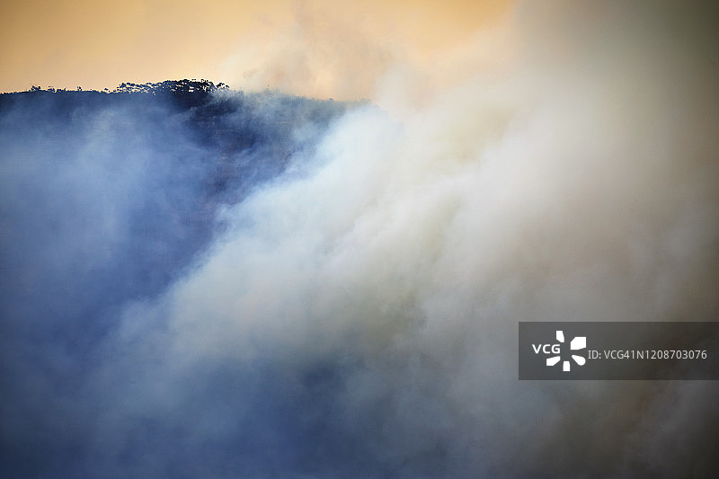 烟雾在山谷从森林火灾与树木成行的山脊图片素材