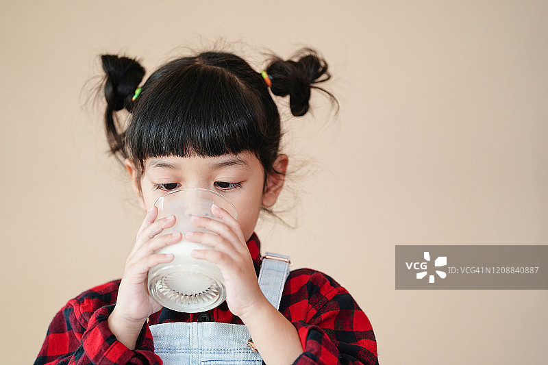 亚洲可爱的小女孩在早上喝着健康的新鲜牛奶。牛奶含有蛋白质、维生素和钙，对儿童的健康非常有益。图片素材