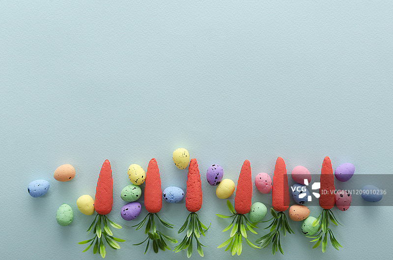 顶视图装饰复活节鹌鹑蛋和小胡萝卜在明亮的蓝色背景。文本空白图片素材